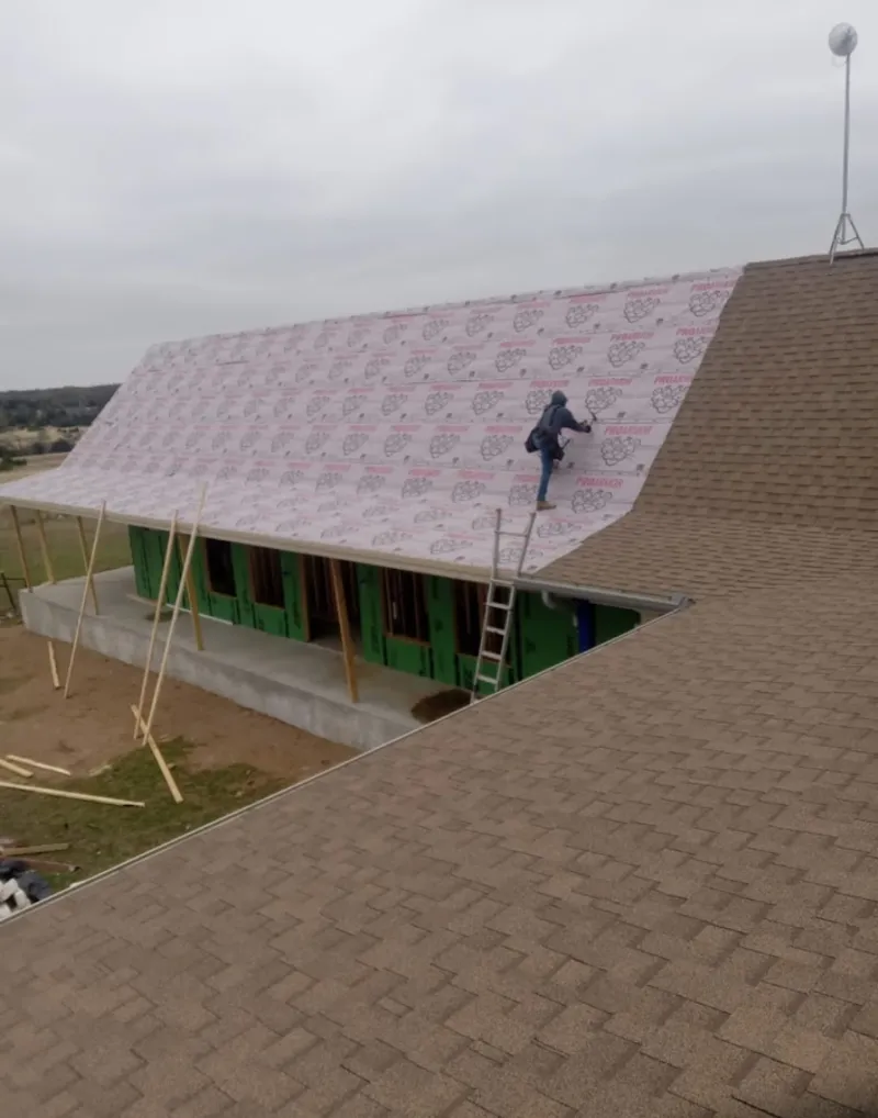 Worker preparing underlayment for a metal roof installation in Ira
